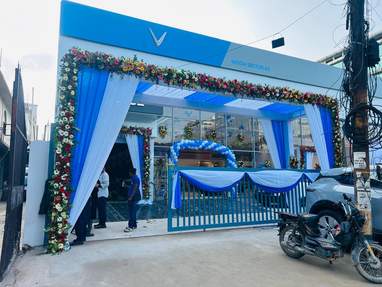 Large blue and white canopy with fresh flower border outside a car showroom in Noida Sector 63